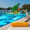 Piscina con scivolo verde e fontana, asciugamano giallo in primo piano.