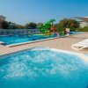 Una piscina con scivoli colorati, vasca idromassaggio in primo piano, lettini e ombrelloni.