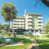 Hotel bianco e verde circondato da un giardino verde con sedie e tavoli all'aperto.