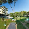 Un giardino con tavolini tra gli alberi, vicino a un edificio bianco a più piani.