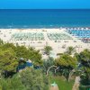 Spiaggia con ombrelloni e lettini vista dal verde di un parco.