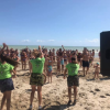 Un gruppo di persone balla sulla spiaggia. Alcuni animatori in maglia verde guidano l'attività.