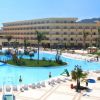 Resort con grande piscina, palme e lettini, edificio a più piani sullo sfondo.