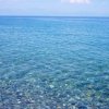 Mare limpido con ciottoli sul fondale e alcune persone in lontananza.