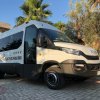 Minibus bianco e nero parcheggiato su un piazzale piastrellato, circondato da palme.