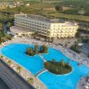 Un ampio hotel con una grande piscina a forma libera e lettini intorno, circondato da vegetazione.