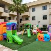 Parco giochi colorato su prato sintetico, con edifici sullo sfondo.