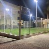 Un campo da padel illuminato di notte con alte recinzioni metalliche.