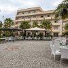 Un cortile con tavoli e sedie bianche, circondato da palme e un edificio a più piani sullo sfondo.