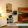 Interno di una camera con scrivania, lampada, sedia, letto a castello e TV.