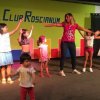Bambini e un adulto che ballano su un palco colorato.