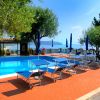 Piscina circondata da sedie a sdraio blu e ombrelloni, con vista mare e alberi.