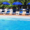 Piscina con sedie a sdraio blu e ombrelloni, circondata da alberi verdi.