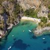 Una piccola baia con acque blu, imbarcazioni e una spiaggia nascosta circondata da scogli.