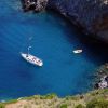 Barca a vela e kayak in mare blu, vicino a una costa rocciosa.