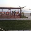 Una terrazza in legno con vista sul mare, circondata da prato e palme.