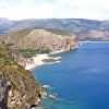Una costa rocciosa con acqua blu e spiagge sabbiose sotto un cielo limpido.