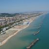 Vista aerea di una lunga spiaggia con ombrelloni e città sullo sfondo.