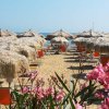 Ombrelloni di paglia e fiori rosa su una spiaggia sabbiosa.