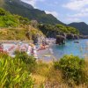 Spiaggia con ombrelloni e mare, circondata da colline verdi.