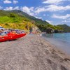 Spiaggia con ombrelloni blu e mare calmo, montagna sullo sfondo.