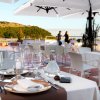 Tavoli apparecchiati su una terrazza, vista su verde e mare.