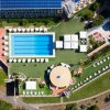 Vista dall'alto di piscina con ombrelloni e giardino.
