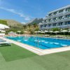 Piscina esterna con lettini e ombrelloni, edificio sullo sfondo.