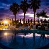 Piscina illuminata al tramonto con palme.