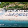 Spiaggia affollata con ombrelloni colorati e auto parcheggiate.
