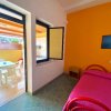 Stanza luminosa con pareti colorate, letto rosa e accesso ad un balcone con tavolo e sedie.