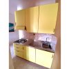 Cucina con mobili gialli, piano cottura, lavabo e rivestimento in marmo.