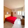 Stanza luminosa con letto matrimoniale e copriletto rosso, finestra e TV.