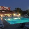 Piscina illuminata di notte, circondata da lettini, con palme e un edificio sullo sfondo.