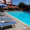 Piscina circondata da lettini blu a righe e ombrelloni, edificio sullo sfondo.