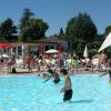 Persone che giocano in una grande piscina all'aperto con sedie a sdraio e ombrelloni intorno.