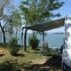 Camper con tenda affacciato su un lago. Sedie sotto l'ombra.