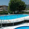 Piscina all'aperto con ponte bianco e area giochi, circondata da alberi e edifici.