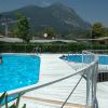 Due piscine con passerella bianca, montagna sullo sfondo. Persone nuotano.