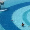 Una piscina a gradiente con una fontana centrale e tre persone che nuotano in acqua.