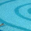 Una piscina con una persona che nuota in solitaria, circondata da anelli concentrici di acqua.