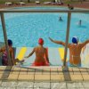 Tre persone sedute sul bordo di una piscina, indossando costumi da bagno e cuffie colorate.