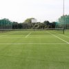 Campo da tennis in erba sintetica circondato da una recinzione verde.
