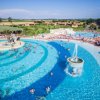 Grande piscina a onde con fontana centrale, palme e persone che nuotano.