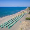 Una spiaggia con file di ombrelloni verdi e gialli, mare azzurro a sinistra.