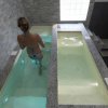 Una donna entra in due vasche rettangolari con acqua trasparente, pareti in pietra grigia.
