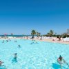 Piscina all'aperto affollata, circondata da sdraio e palme.