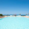 Piscina tranquilla all'aperto, circondata da lettini bianchi e vista sul mare. Cielo limpido.
