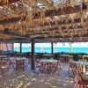 Un ristorante all'aperto con tavoli e sedie di legno, tetto di paglia e vista sul mare.