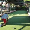 Due persone giocano a bocce su un campo erboso coperto da un pergolato.